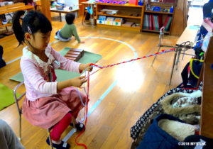 毛糸の束で三つ編みの練習をする子