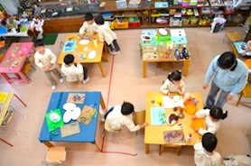 ピンク、青などの机の周りでお仕事をする子どもたち。恵泉幼稚園の教室の様子。