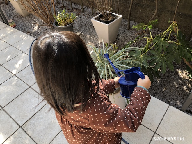 外の植木に水やりをする子供