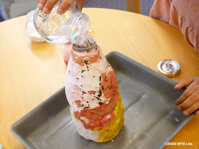 モンテッソーリ教育の地理学で噴火を学ぶため洗剤と重曹の入った容器に酢を入れる様子