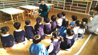 瀬高大谷幼稚園で地球儀を持った先生の話を正座して聞く子どもたち