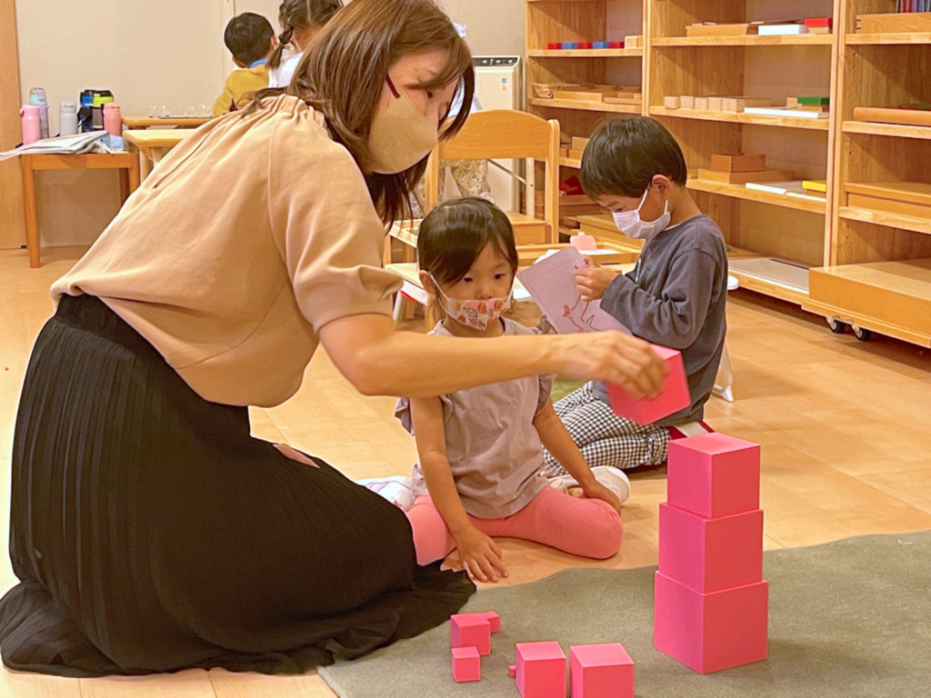 3歳の女の子にピンクのブロックを大きい順に積む様子を見せる女の先生